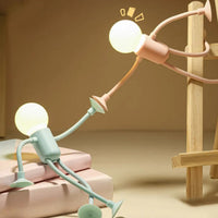Groen en roze mannetjeslampje bij elkaar: het groene zit op boeken en reikt omhoog, het roze hangt aan een houten ladder. 6