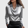 Model draagt de glanzende satijnen blouse in zilvergrijs met gedrapeerde hals en kraag, gecombineerd met een zwarte rok en strassketting. 2
