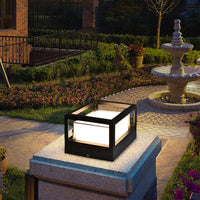 Vierkante zwarte lamp met open kooidak op een granieten tuinpilaar, met bloemperken en een fontein op de achtergrond. 2