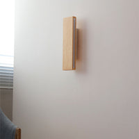 Uitgeschakelde houten wandlamp in verticale stand aan een witte muur, zijaanzicht naast een raam met jaloezie. 2