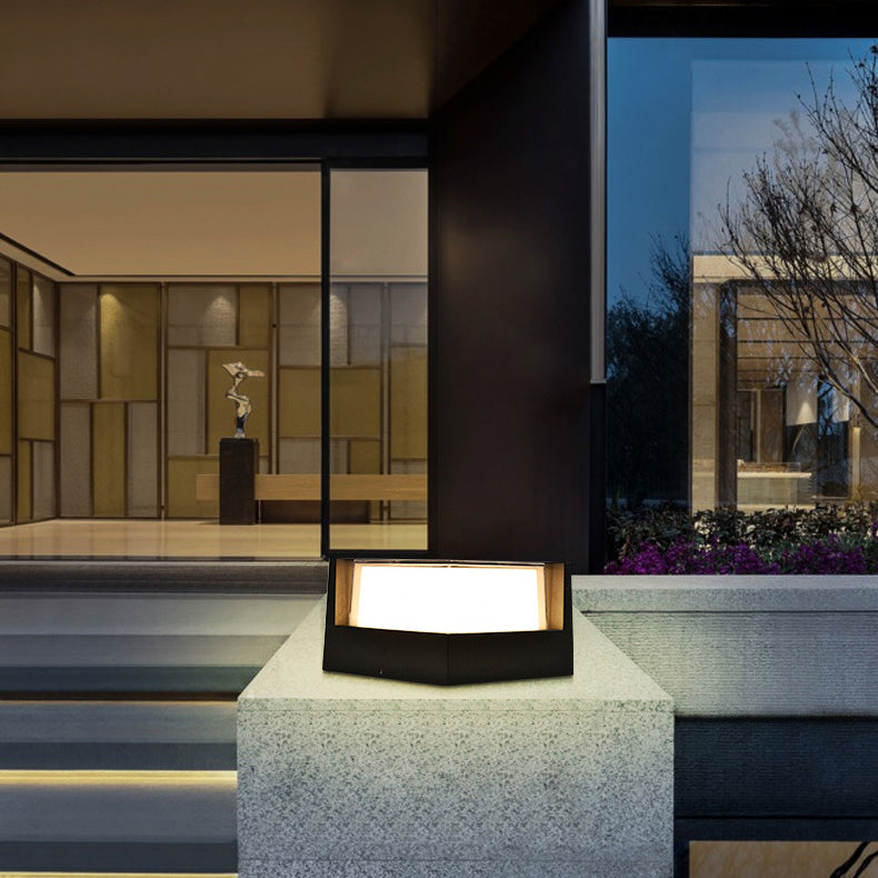 Zwarte lamp met verlichte lichtkap op een betonnen sokkel voor een modern huis met grote glazen pui. 3