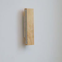 Uitgeschakelde houten wandlamp in verticale stand met zichtbare matte lichtstrip aan de zijkant en witte steun erachter. 11