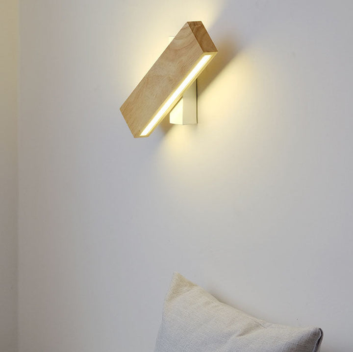 Houten ledwandlamp met witte steun, schuin gedraaid en brandend aan een witte muur boven een kussen. 1