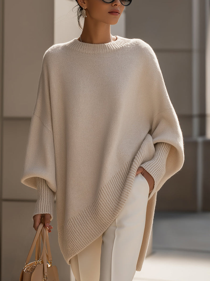 Beige gebreide poncho gedragen door een model met zonnebril en tas, voorkant bij gebouwen 2