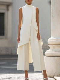 Crèmekleurige set met asymmetrische mouwloze top en wijde broek, vooraanzicht op een model naast een witte zuil. 3