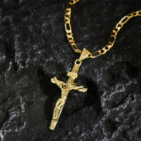 Gouden crucifixhanger met Figaro-ketting liggend op donker, ruw gesteente 9