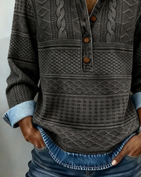 Detail van de grijze sweatshirt met knoopsluiting, reliëfpatroon in banen en een denim onderrand boven een spijkerbroek. 7