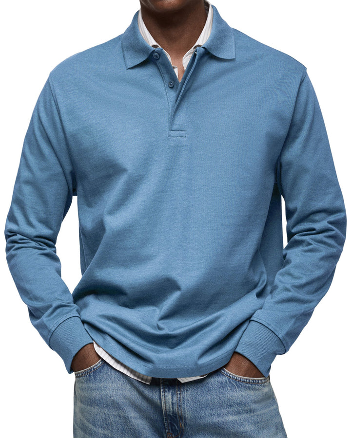 Man draagt het poloshirt met lange mouwen in een middenblauwe kleur, over een gestreept overhemd en met een spijkerbroek. 2