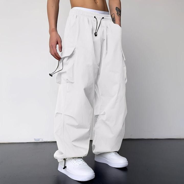 Model draagt de wijde cargobroek in wit met zijzakken en elastische enkelboorden, gecombineerd met witte sneakers 4
