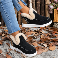 Zwarte instapsneakers met pluchen rand, wit zoolrandje en sierstiksels, gedragen met spijkerbroek tussen herfstbladeren, zijaanzicht. 1