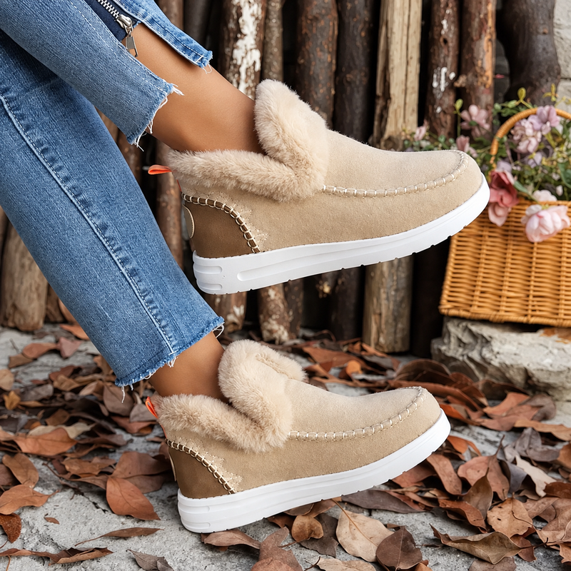 Beige suèdelook instapsneakers met pluchen rand en witte zool, gedragen met spijkerbroek bij houten palen en een rieten mand. 3
