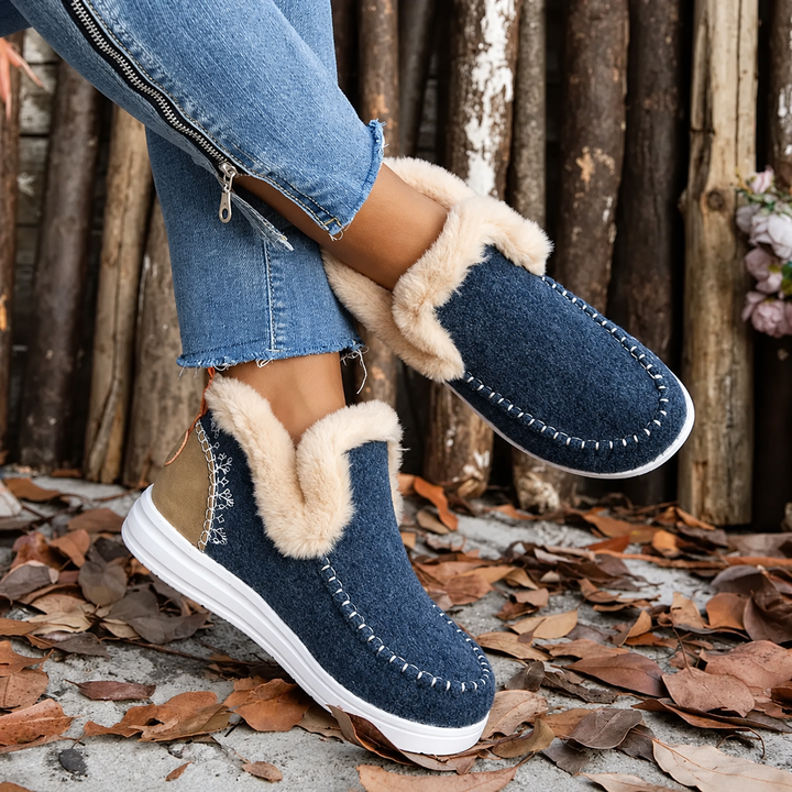 Blauwe instapsneakers met pluchen rand en bruin hielstuk, gedragen met gekruiste benen, zijaanzicht met zichtbare sierstiksels. 4