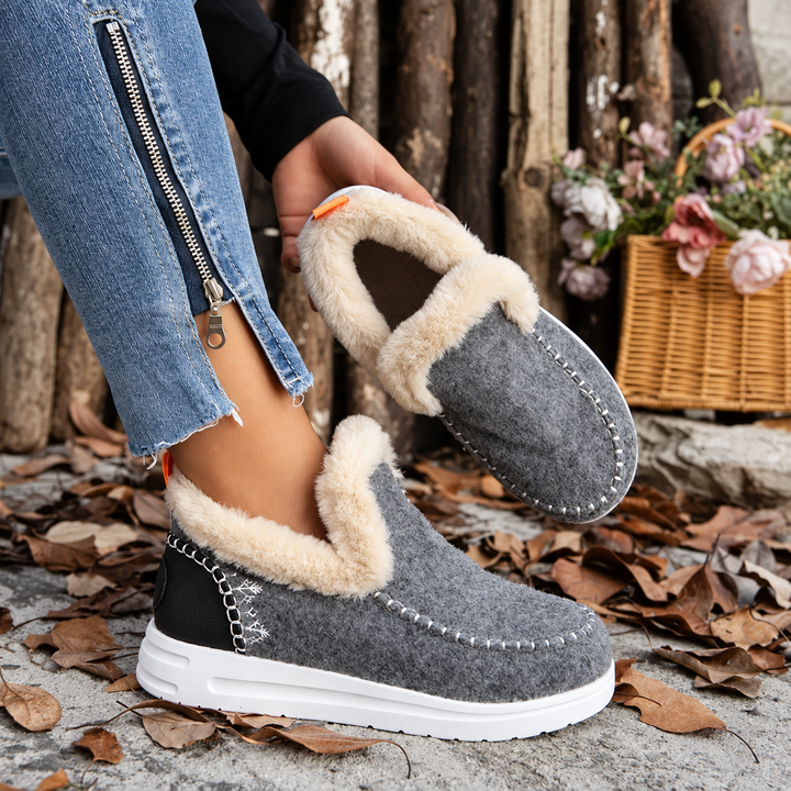 Grijze instapsneakers met pluchen voering; het model houdt één schoen omhoog zodat de zachte binnenkant zichtbaar is. 5