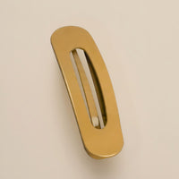 Matte okergele haarclip met ovale opening, schuin van boven gefotografeerd op een beige achtergrond 12