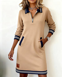 Beige jurk met ritskraag en gestreepte zoom, model met hand in de zak, volledig frontaal. 9