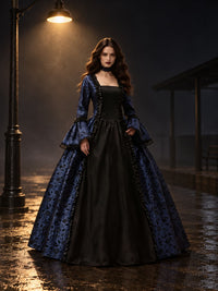 Model in blauwe jurk met zwart middenpaneel en uitlopende mouwen, 's nachts onder een straatlantaarn op nat plaveisel. 1