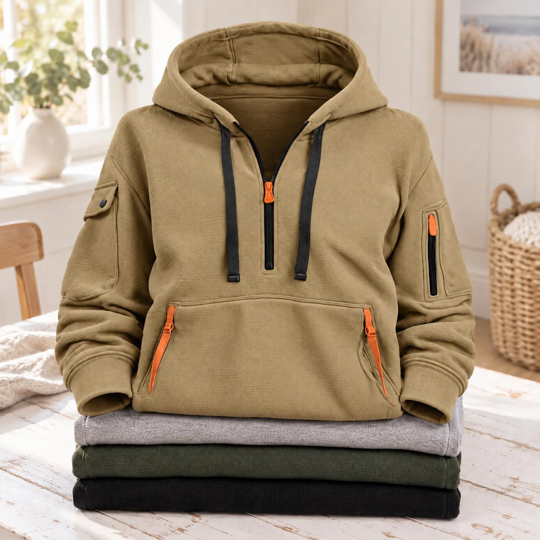 Zandkleurige hoodie met halve rits, zwarte koorden en oranje ritsen, bovenop gevouwen truien 4
