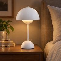 Witte paddenstoelvormige lamp brandt met warm licht op een houten nachtkastje naast een glas water en bed 1