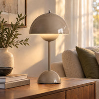 Glanzend taupekleurige tafellamp met zacht warm licht, op een houten dressoir naast een bank 9