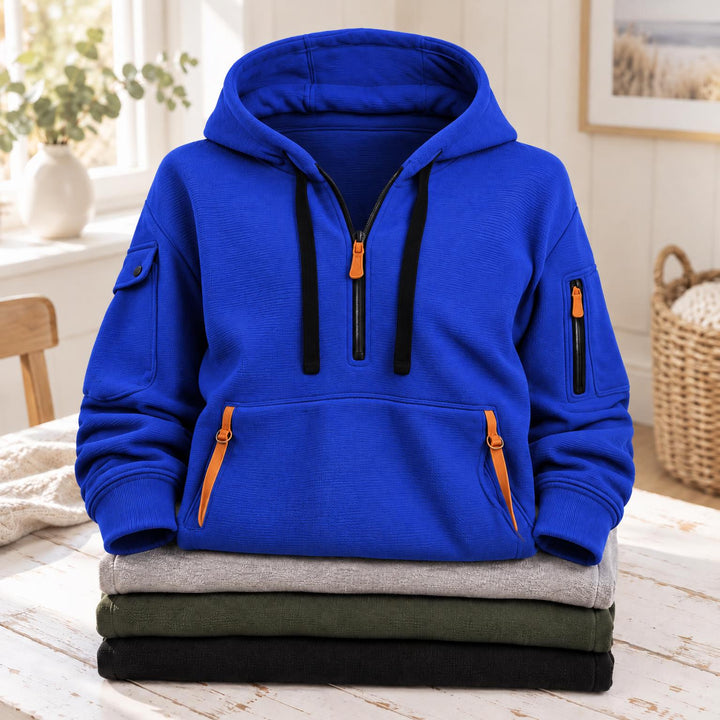 Felblauwe hoodie met halve rits, oranje ritsen en zwarte koorden, op een stapel truien 9