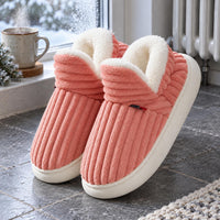 Paar roze geribbelde sloffen met witte pluche voering op een tegelvloer naast een radiator 6