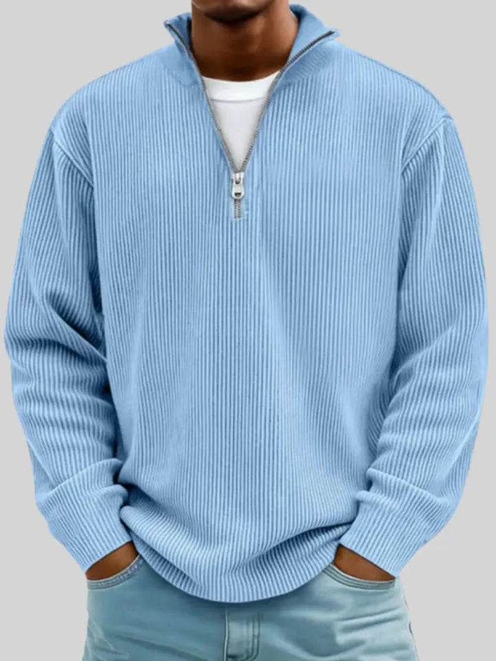 Model draagt de geribbelde trui met kwartrits in lichtblauw, met een wit shirt eronder en handen in de zakken van een spijkerbroek. 1