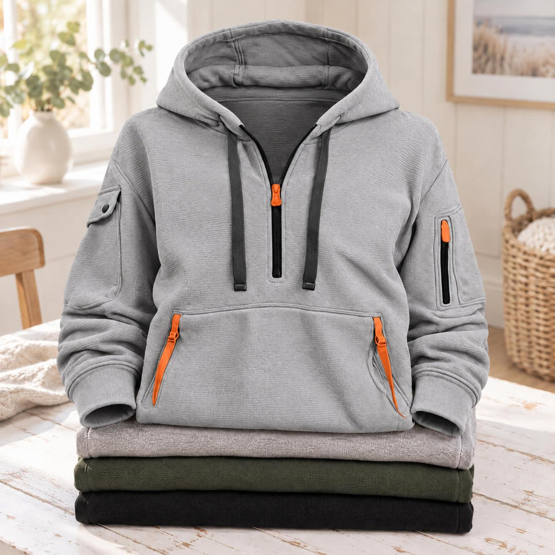 Lichtgrijze hoodie met halve rits, oranje ritsen en donkere koorden, op een gevouwen stapel 3