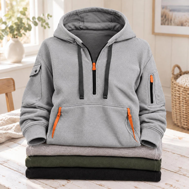 Lichtgrijze hoodie met halve rits, oranje ritsen en donkere koorden, op een gevouwen stapel 3