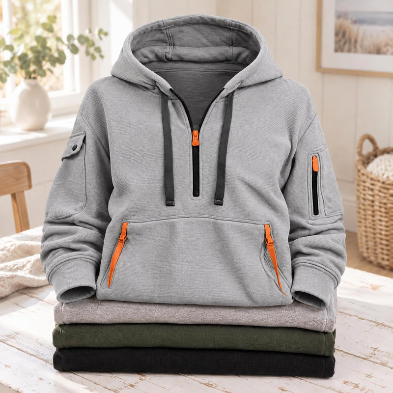 Lichtgrijze hoodie met halve rits, oranje ritsen en donkere koorden, op een gevouwen stapel 3