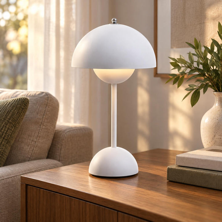 Witte paddenstoelvormige tafellamp met warm licht op een houten dressoir naast een bank en plant 1