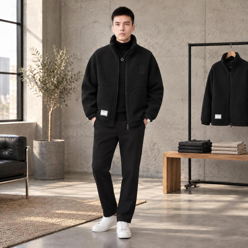 Model in een betonnen loft draagt de zwarte fleecejas met zwarte broek en witte sneakers 2