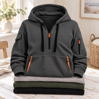 Donkergrijze hoodie met oranje ritsen en zwarte koorden, liggend op een stapel truien 6