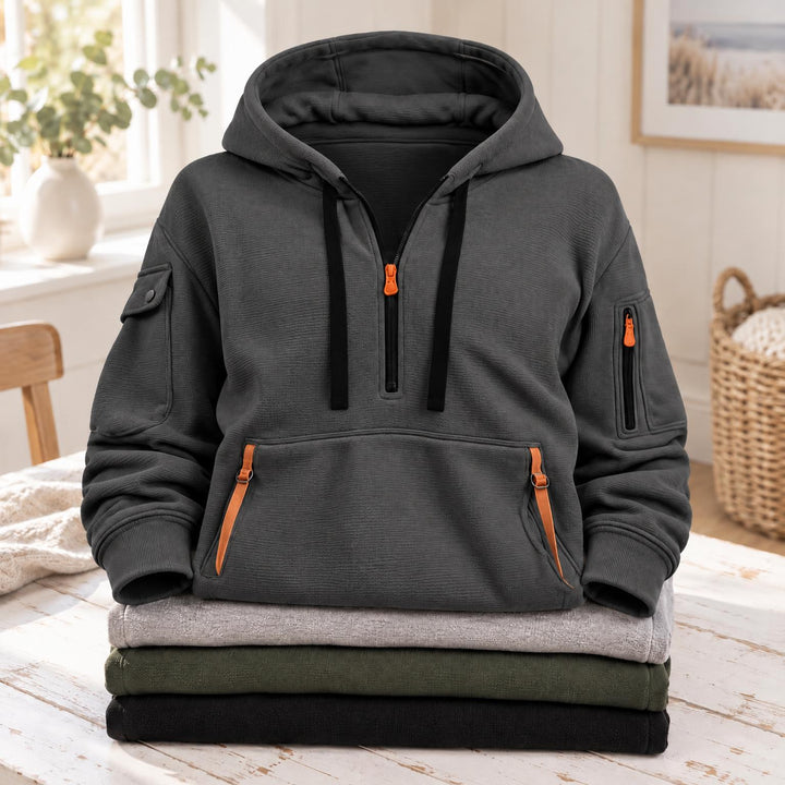 Donkergrijze hoodie met oranje ritsen en zwarte koorden, liggend op een stapel truien 6