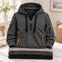 Donkergrijze hoodie met oranje ritsen en zwarte koorden, liggend op een stapel truien 6