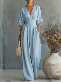 Model draagt de lichtblauwe jumpsuit, met een rieten handtas en droogbloemen in een vaas op de achtergrond 7