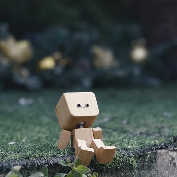 Houten figuurtje met lachend gezichtje zit op kunstgras in de tuin, met wazige lichtjes op de achtergrond. 5