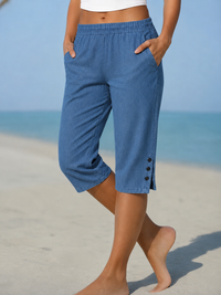 Model op het strand draagt de capribroek in middenblauw denimlook, met handen in de zijzakken 3
