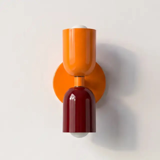 Wandlamp met een oranje bovenkap en een donkerrode onderkap op een oranje ronde wandplaat, tegen een lichte muur. 25