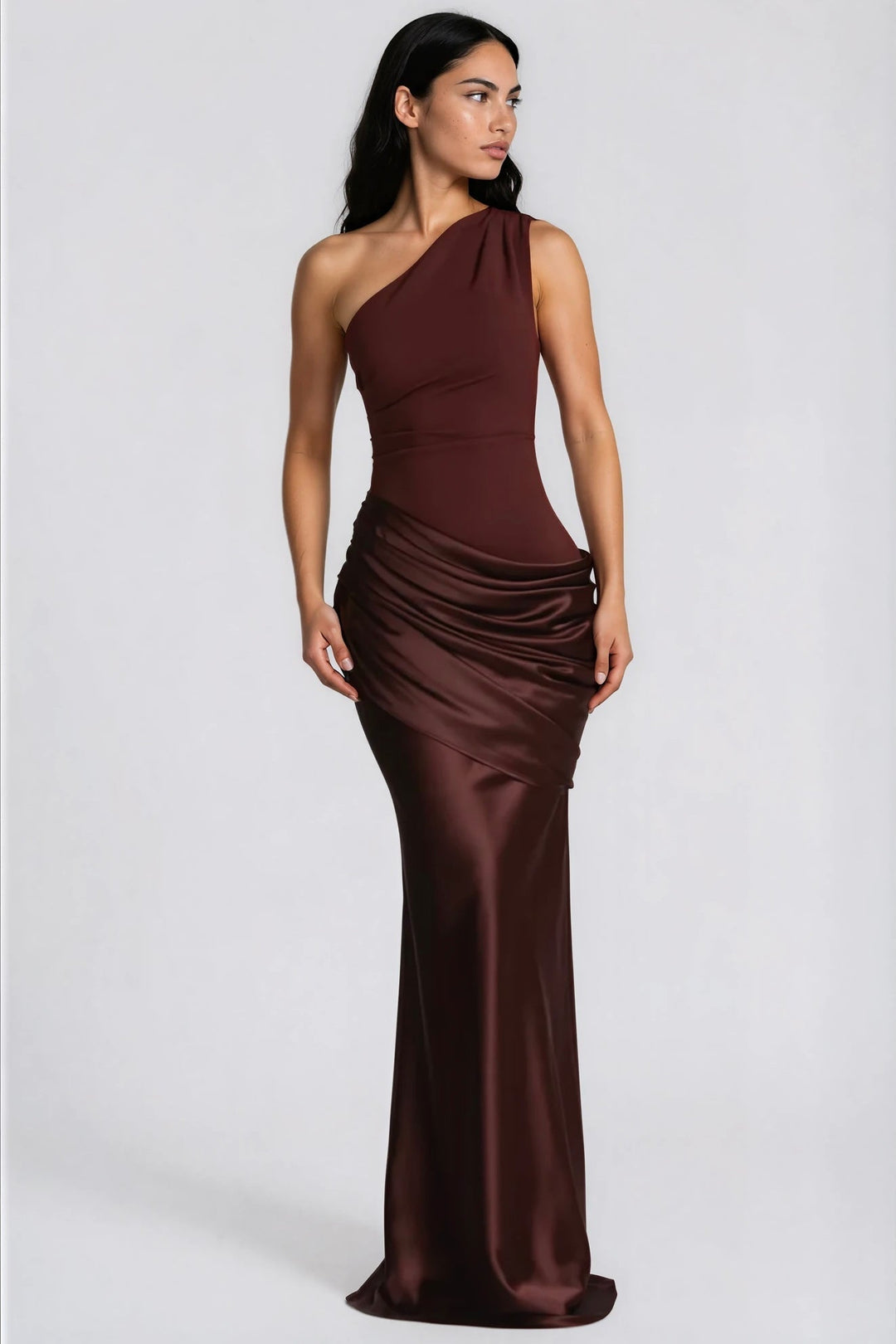 Model in donkerbruine maxi-jurk, driekwartsaanzicht, met gedrapeerde glanzende satijnen heup en één blote schouder. 6
