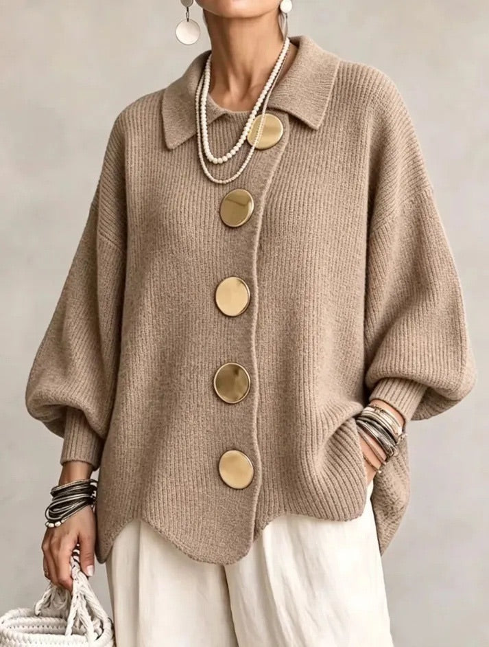 Model draagt het gebreide vest in taupe met gouden knopen, ballonmouwen en een witte broek, vooraanzicht. 7