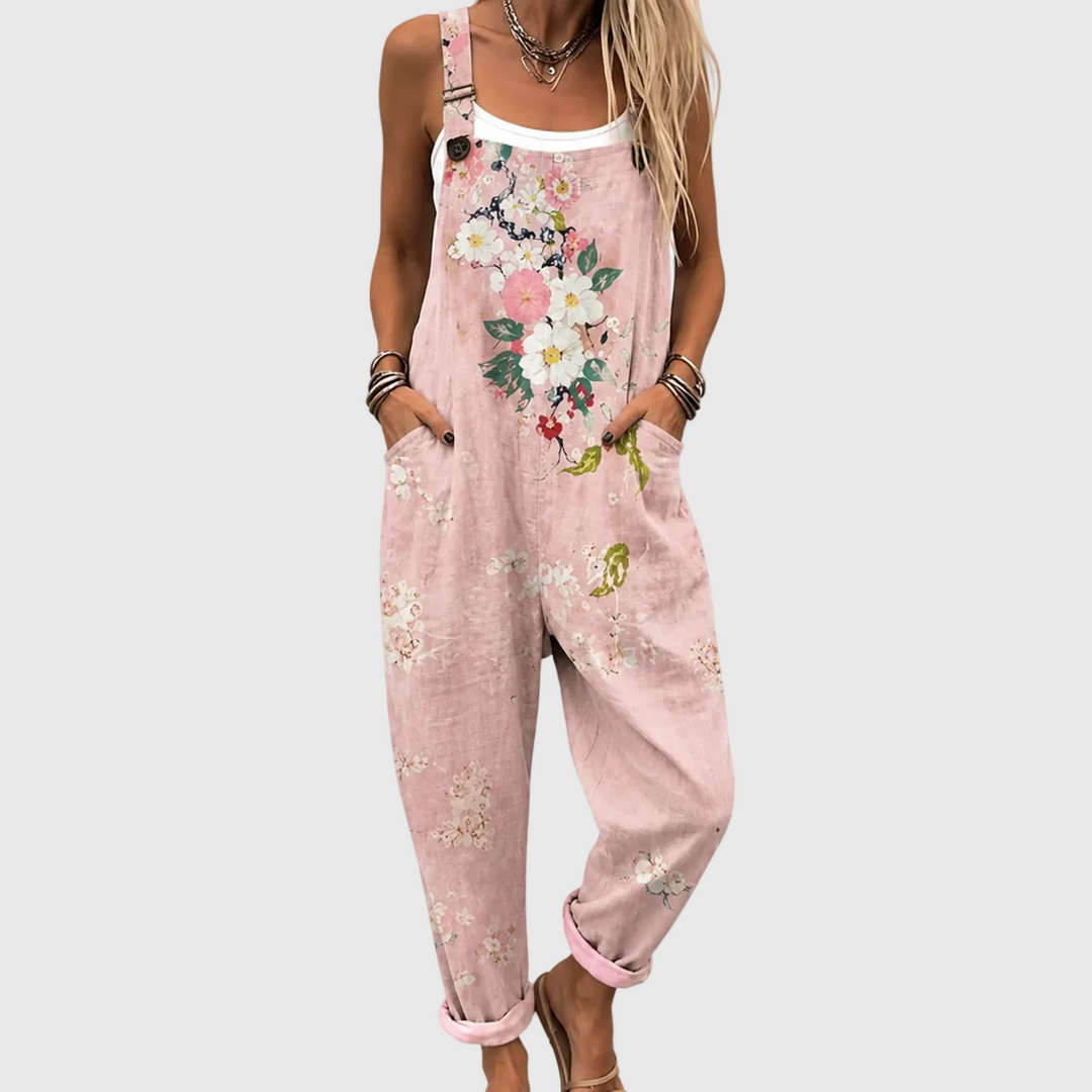 Close-up van het bovenlijf: model draagt de roze tuinbroek met bloemenprint over een wit topje, handen in de zijzakken. 1