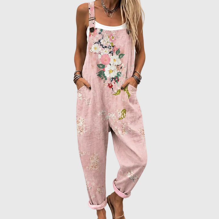 Close-up van het bovenlijf: model draagt de roze tuinbroek met bloemenprint over een wit topje, handen in de zijzakken. 1