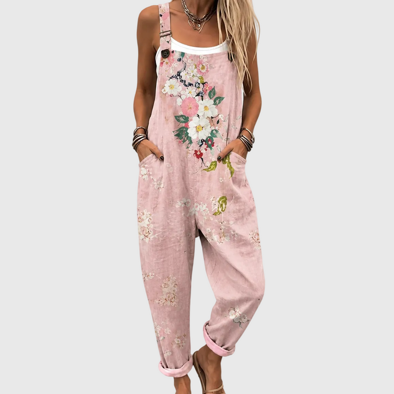 Close-up van het bovenlijf: model draagt de roze tuinbroek met bloemenprint over een wit topje, handen in de zijzakken. 1