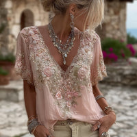 Tweede kijk op de roze blouse in vierkant beeld, met de borduurbloemen en kanten mouwranden, gedragen voor een stenen muur met roze bloemen. 2