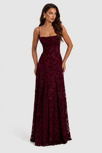 Model in bordeauxrode jurk met reliëfbloemen, gedrapeerde halslijn en dunne bandjes, vooraanzicht met gouden oorbel. 9