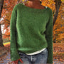 Vrouw draagt de gebreide trui in groen over een wit shirt en spijkerbroek, met herfstkleuren op de achtergrond. 5
