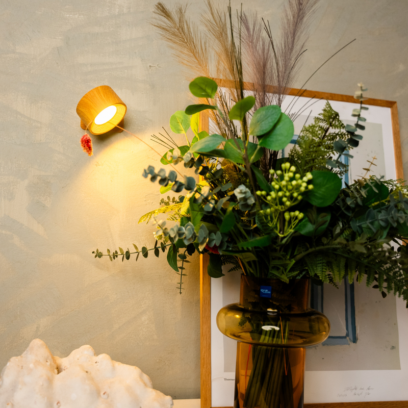 Houtlook wandlamp brandt naast een boeket van eucalyptus, varens en pampasgras in een bruine glazen vaas. 6