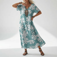 Model draagt de jurk in turquoise met een witte bloesemprint over de hele jurk, met statement-ketting en zwarte sandalen. 4