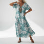 Model draagt de jurk in turquoise met een witte bloesemprint over de hele jurk, met statement-ketting en zwarte sandalen. 4