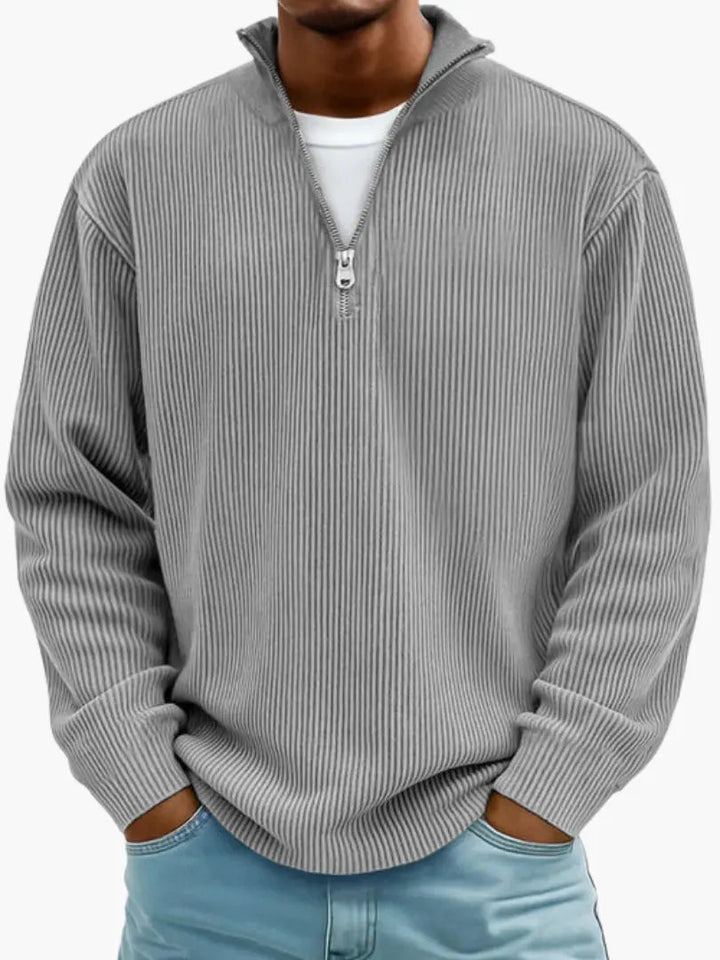 Dezelfde geribbelde trui met opstaande kraag en kwartrits in grijs, gedragen over een wit shirt en een lichtblauwe spijkerbroek. 2